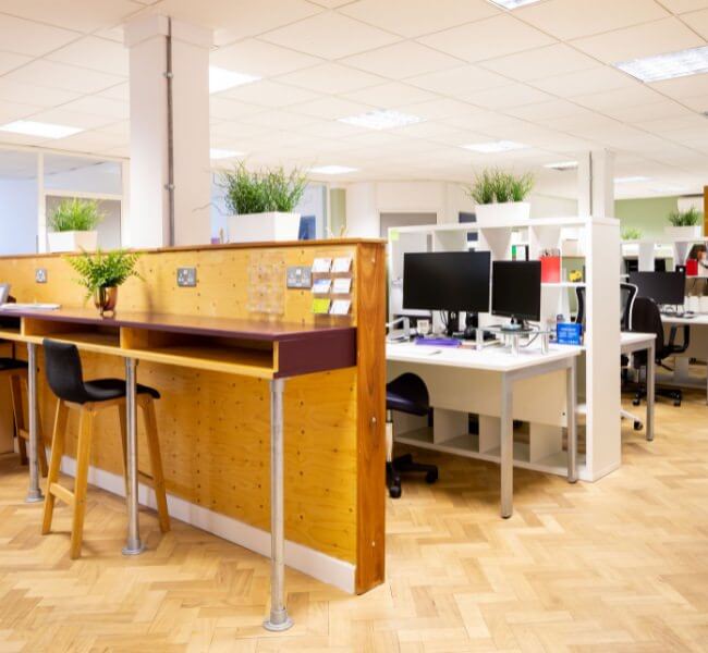 coworking space showing desks with laptops screens and desks with a wooden bar area