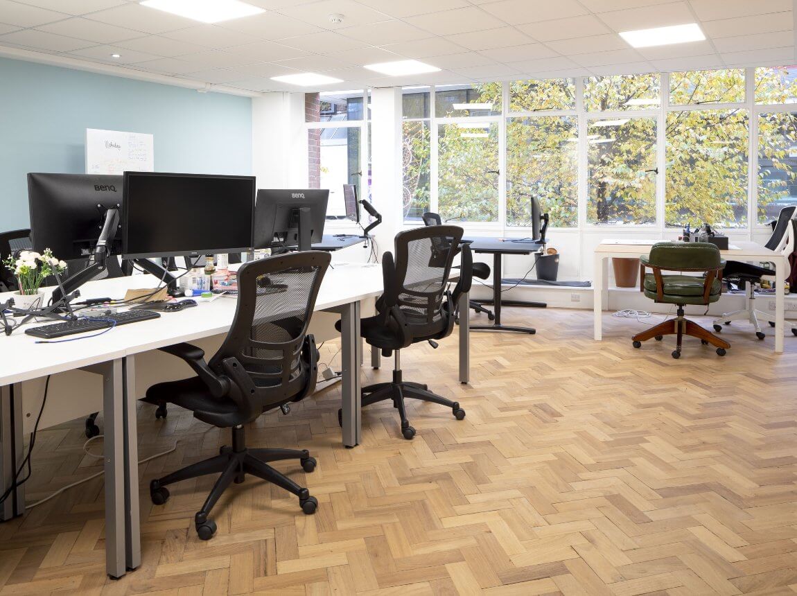Serviced office in woking with multiple desks, chairs and screens for business use with a large window and tree behind