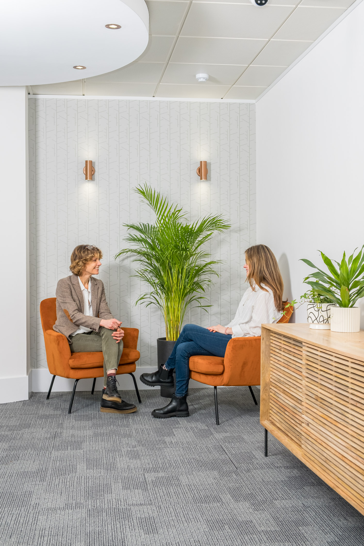 Two people sitting in orange chairs in a breakout space, chatting and collaborating in a coworking area